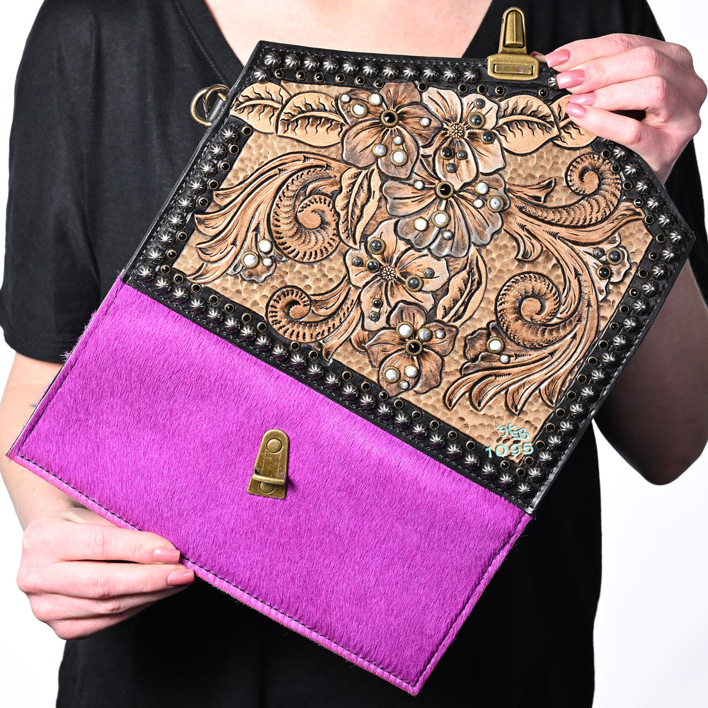 
                  
                    Person holding a Heritage Brand nola clutch #1095 with floral embossing and a bright pink lower half.
                  
                