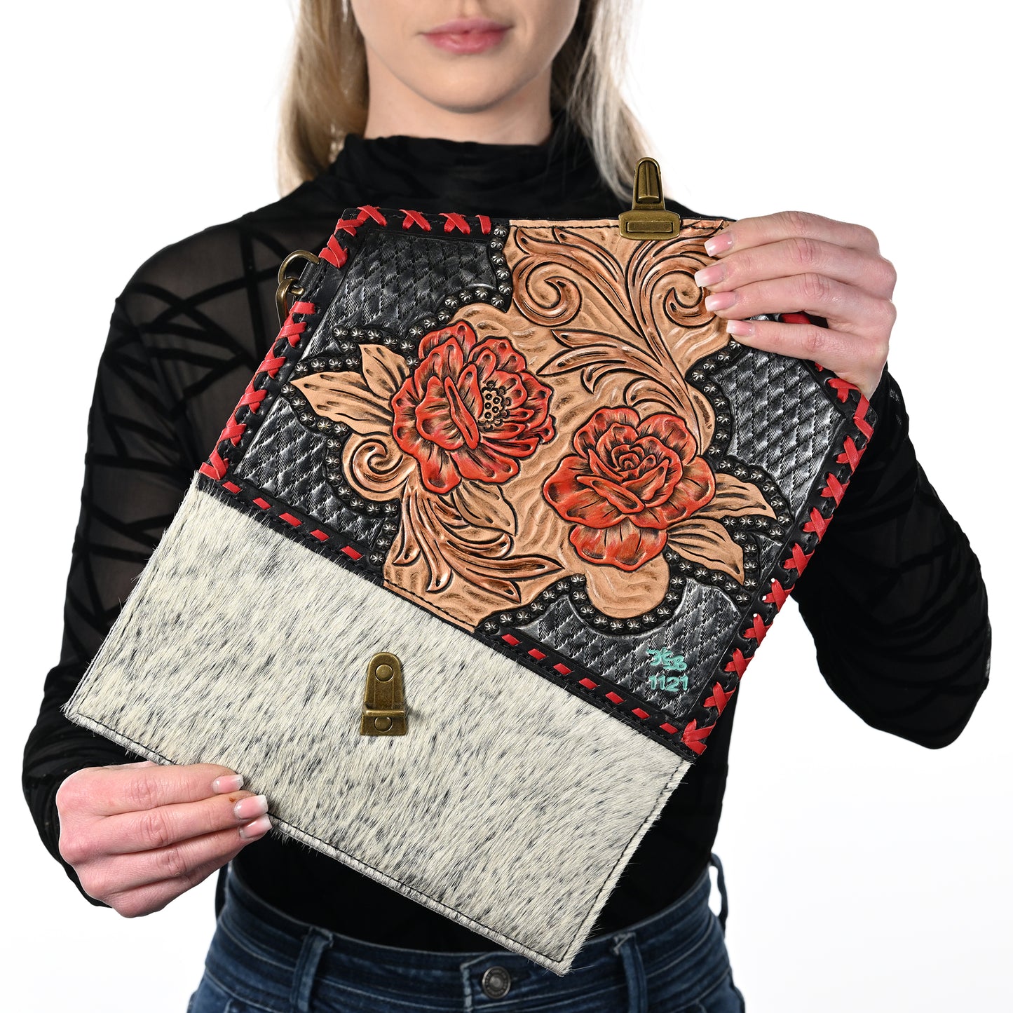 
                  
                    Woman holding a Heritage Brand nola clutch #1127 with floral design and hair-on-hide texture.
                  
                