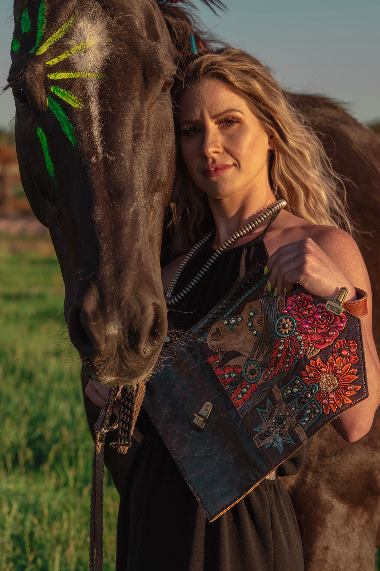 
                  
                    A woman standing close to a horse, holding a Heritage Brand nola clutch #708, with a field in the background.
                  
                