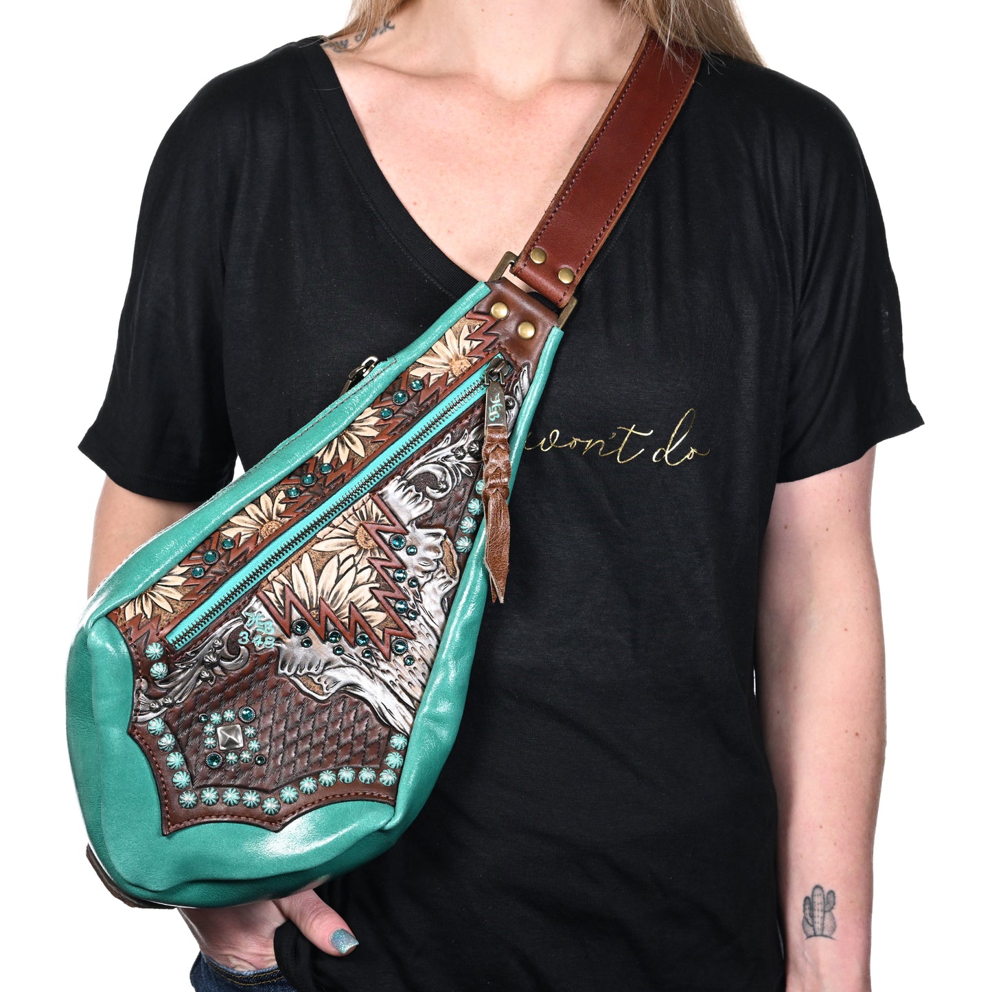 
                  
                    A person wearing a black t-shirt with cursive text and carrying a Heritage Brand fyra bag #348 in teal and brown pattern.
                  
                