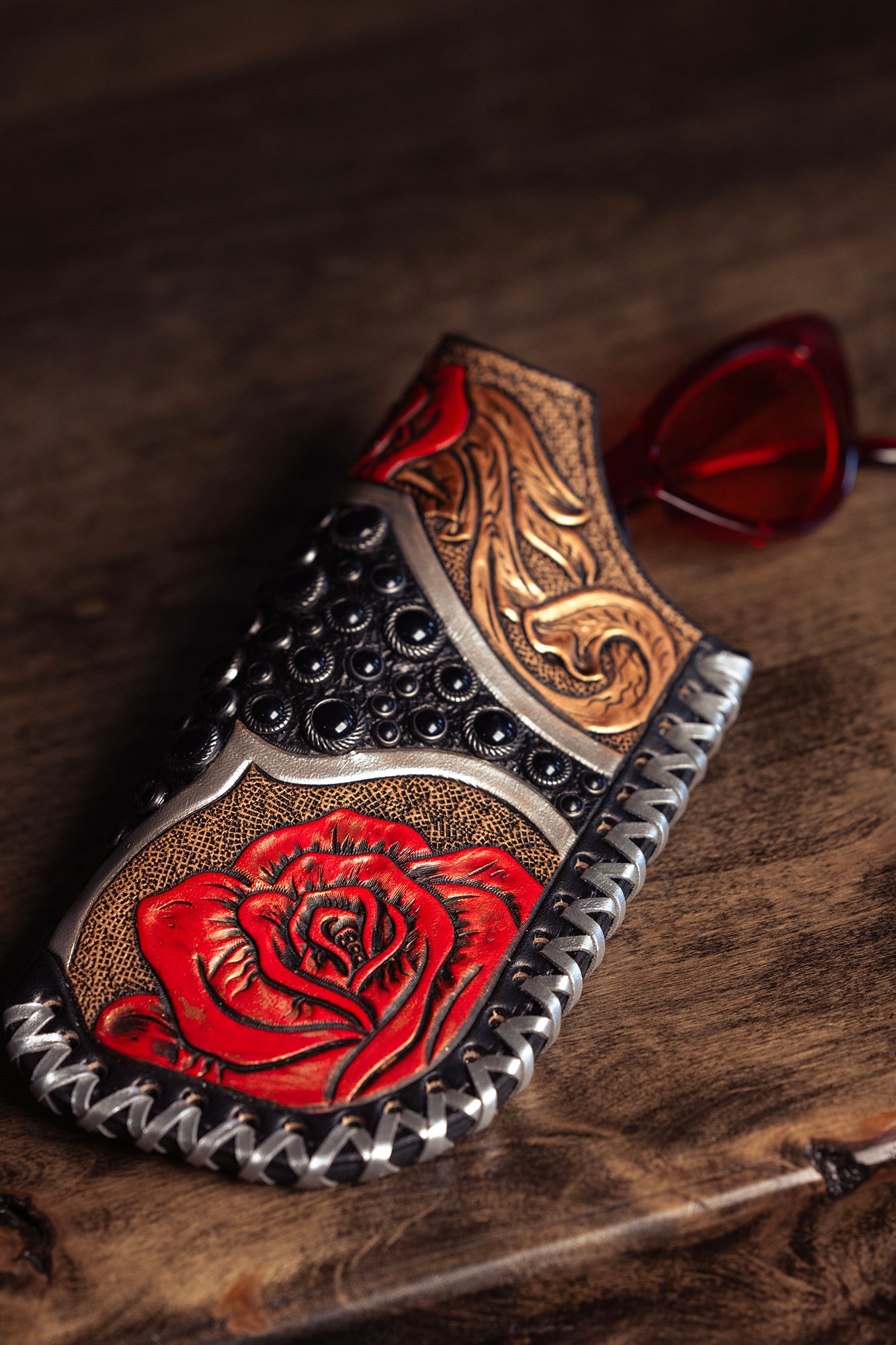 
                  
                    hand-tooled slip-on shoe with rose design next to Heritage Brand shayde case #159 on a wooden surface.
                  
                