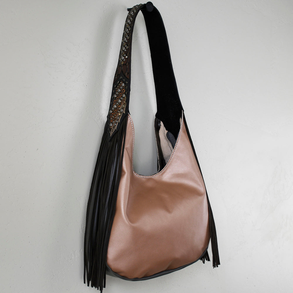 A beige Heritage Brand marilyn bag #4 with black fringe detail hanging against a white wall.