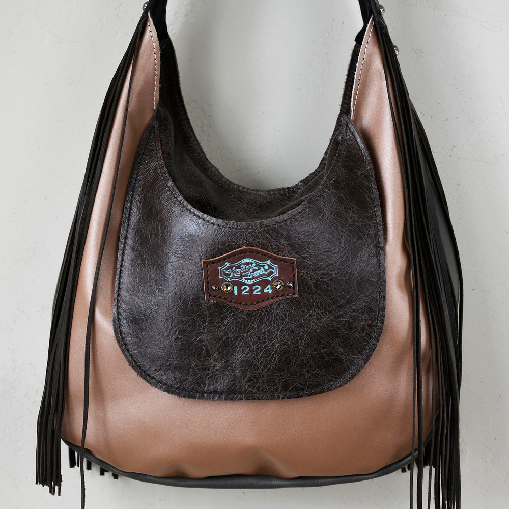 
                  
                    Marilyn bag #4 by Heritage Brand with fringe and a logo patch hanging on a white wall.
                  
                