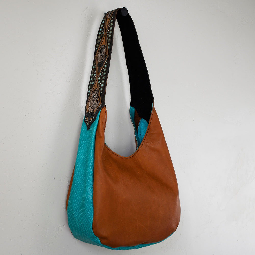 
                  
                    Brown and teal Marilyn Bag #19 by Heritage Brand with patterned strap hanging against a white wall.
                  
                
