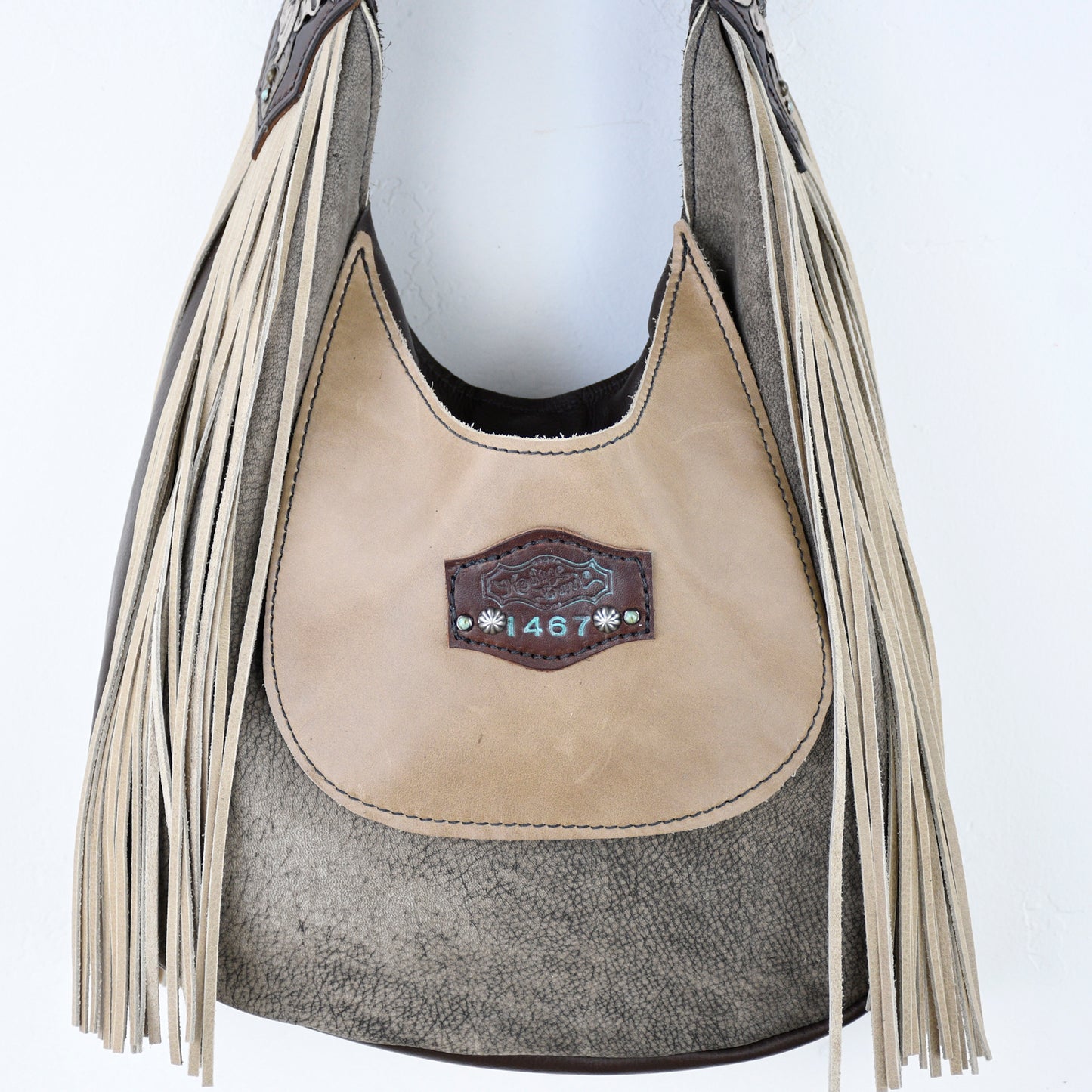 
                  
                    A two-tone fringe Marilyn bag #696 by Heritage Brand hanging against a white wall.
                  
                