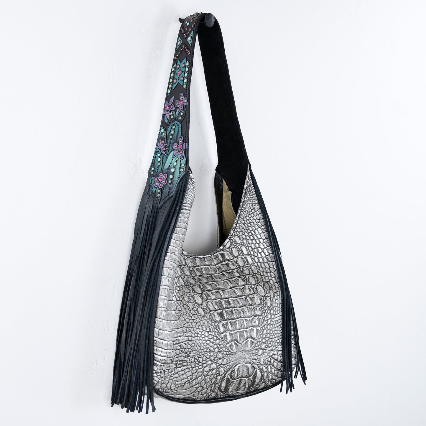 
                  
                    A silver crocodile patterned Marilyn bag #858 with black fringe and a floral strap against a white background by Heritage Brand.
                  
                