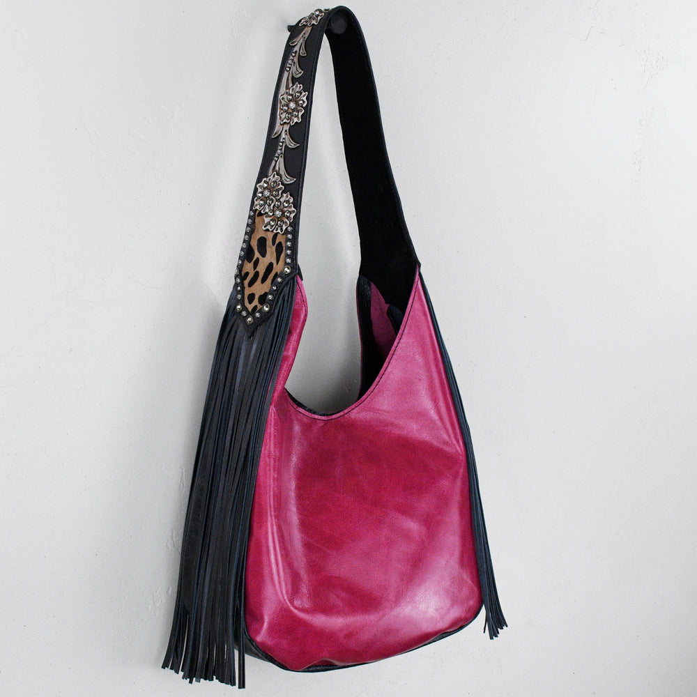 A pink leather marilyn bag #25 with black fringe and a decorative strap hanging on a white wall by Heritage Brand.