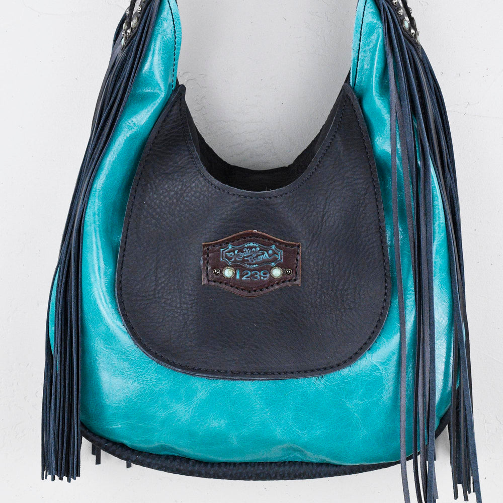 
                  
                    Marilyn bag #26 by Heritage Brand, a black and turquoise leather handbag with fringe detail hanging against a white background.
                  
                