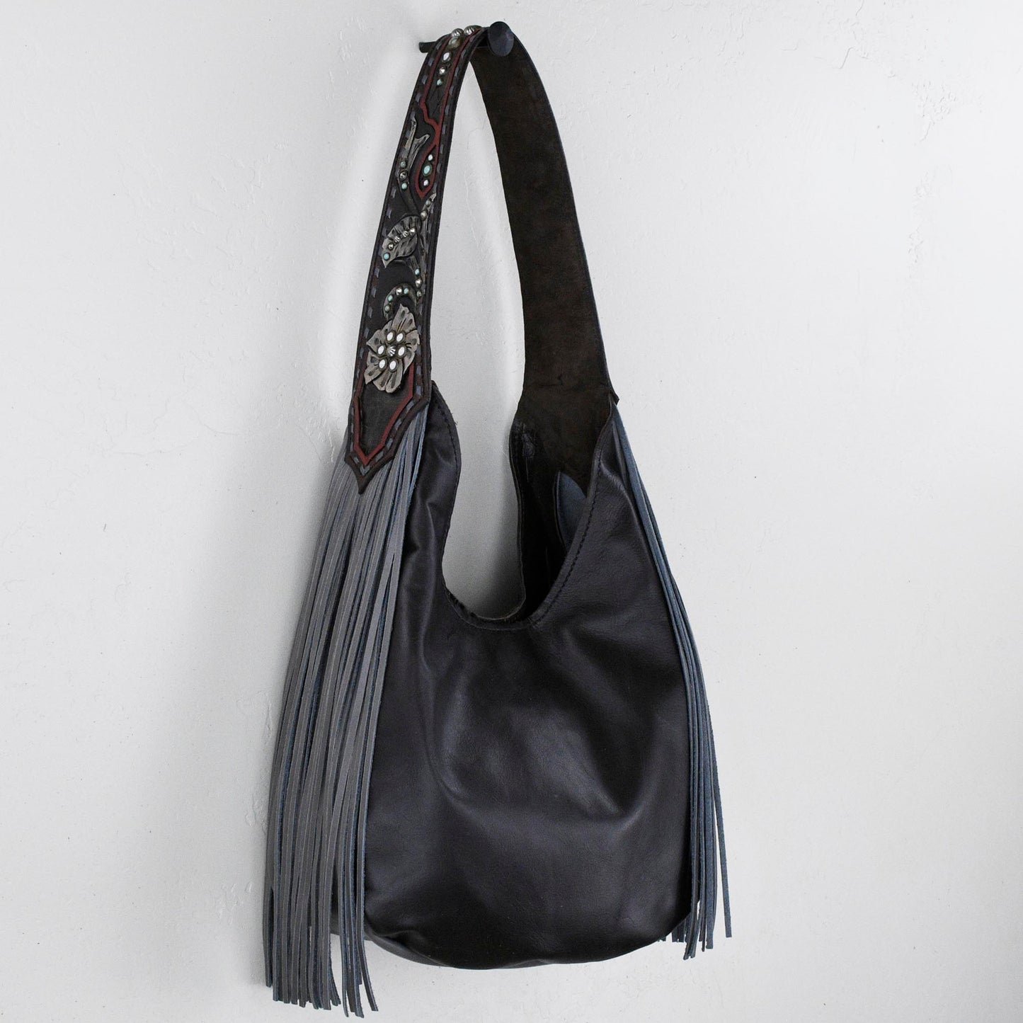 
                  
                    A black marilyn bag #27 with fringes on a white wall by Heritage Brand.
                  
                