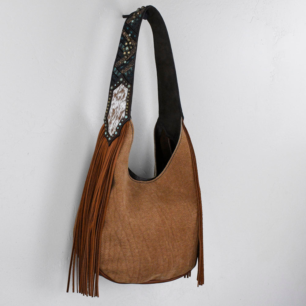 
                  
                    Marilyn bag #28 by Heritage Brand, with fringe detail and patterned strap hanging on a white wall.
                  
                