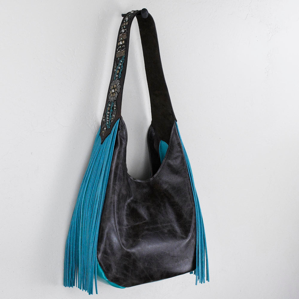 Black and blue Marilyn bag #29 with fringe detail hanging on a white wall by Heritage Brand.