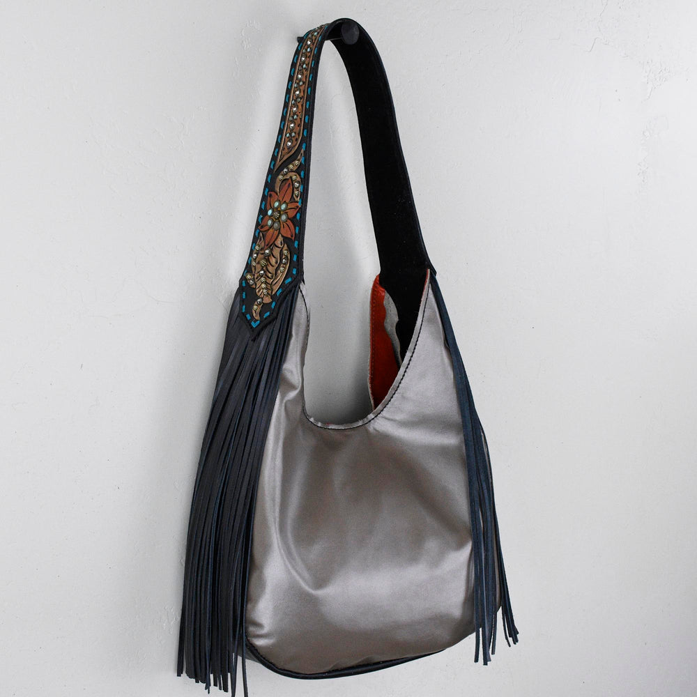
                  
                    Marilyn bag #31 with fringe and decorative strap hanging against a white wall.
                  
                