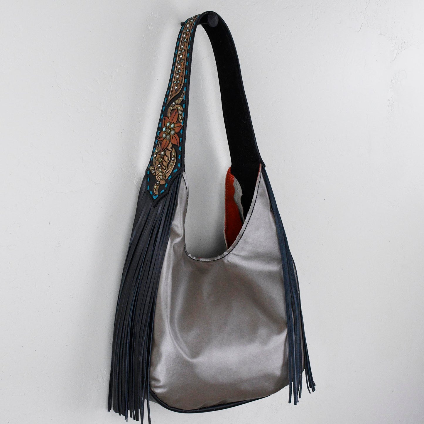 
                  
                    Marilyn bag #31 with fringe and decorative strap hanging against a white wall.
                  
                