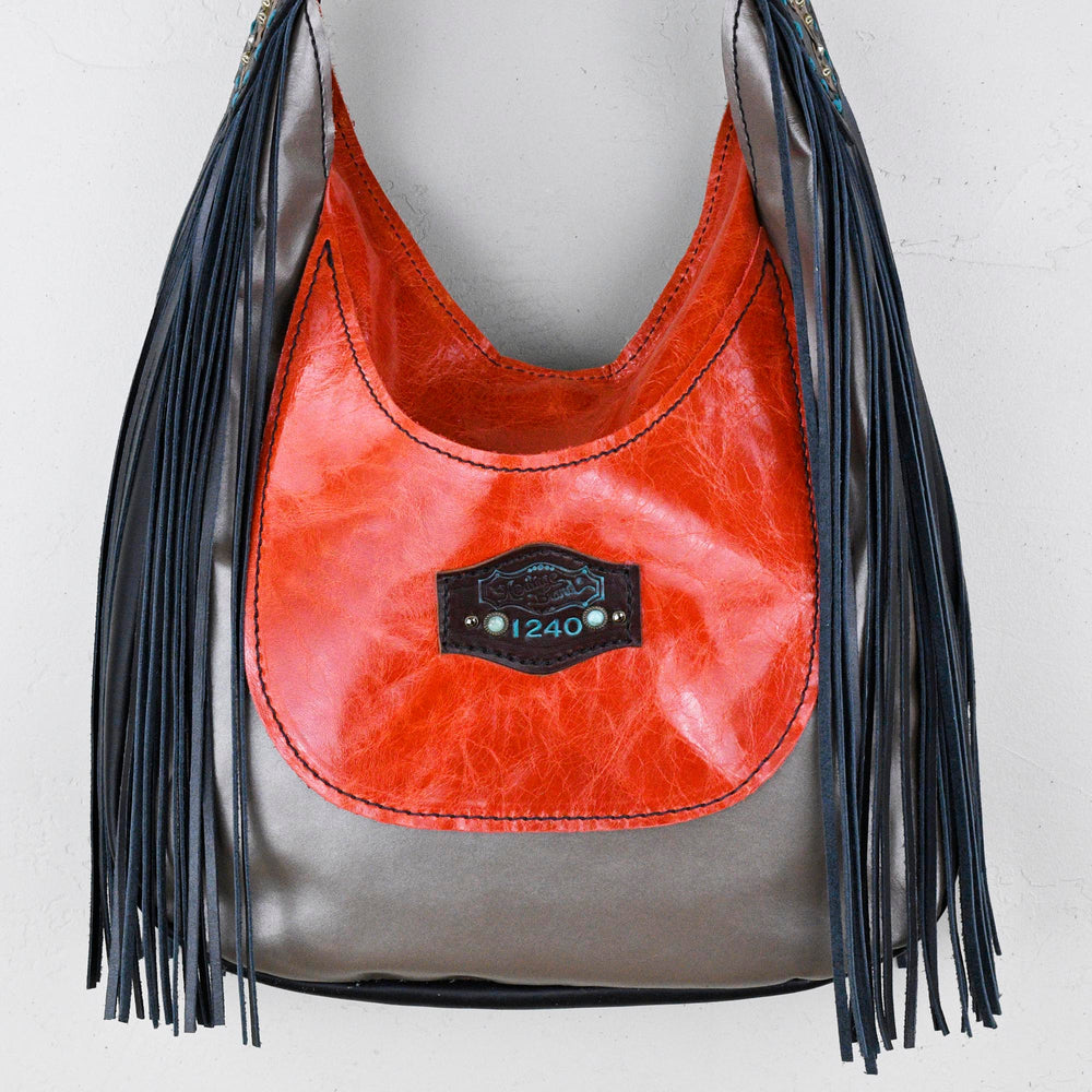 
                  
                    A red and grey leather Marilyn bag #31 with fringe detail hanging against a white wall by Heritage Brand.
                  
                
