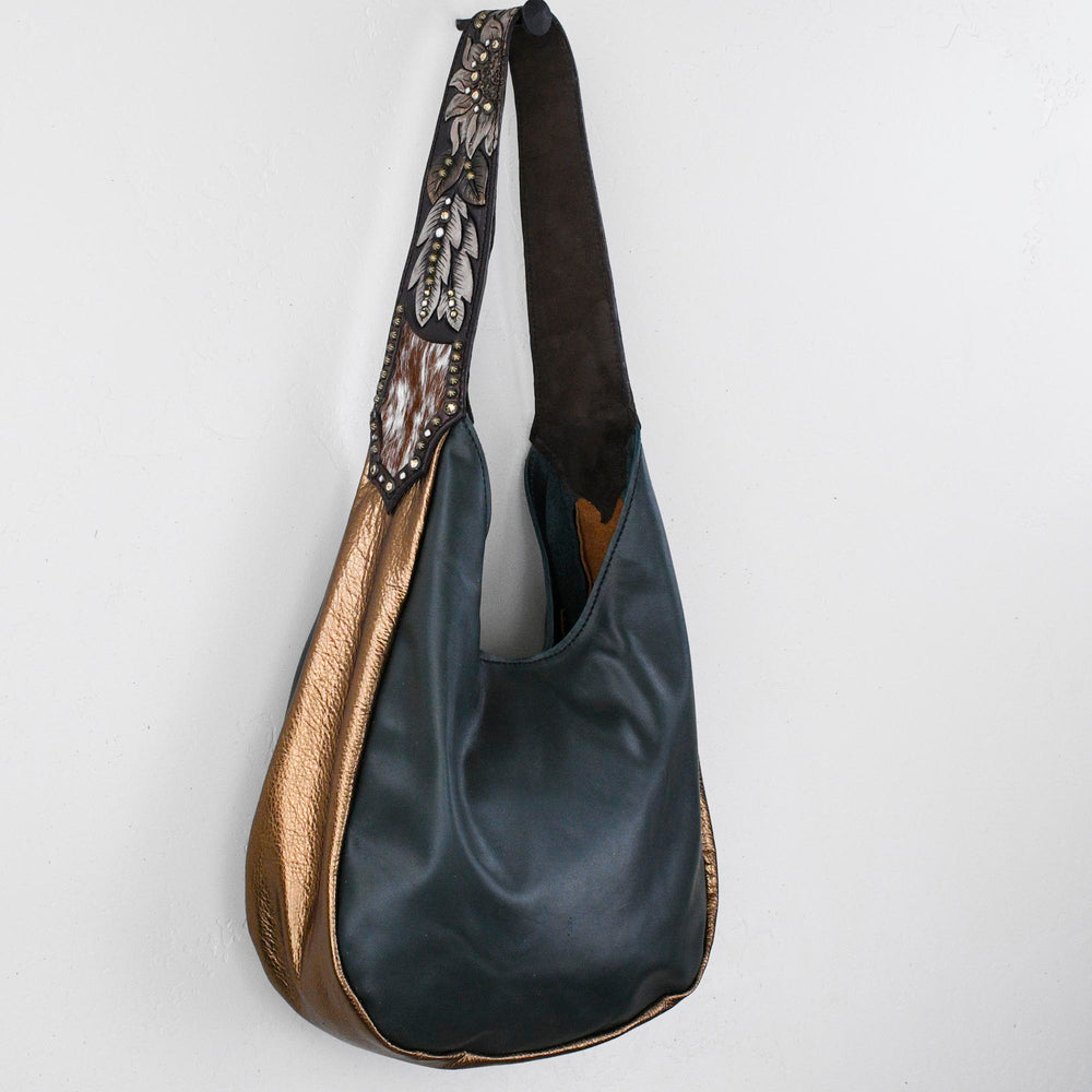 
                  
                    A black and gold Marilyn bag #36 shoulder bag hanging against a white wall by Heritage Brand.
                  
                