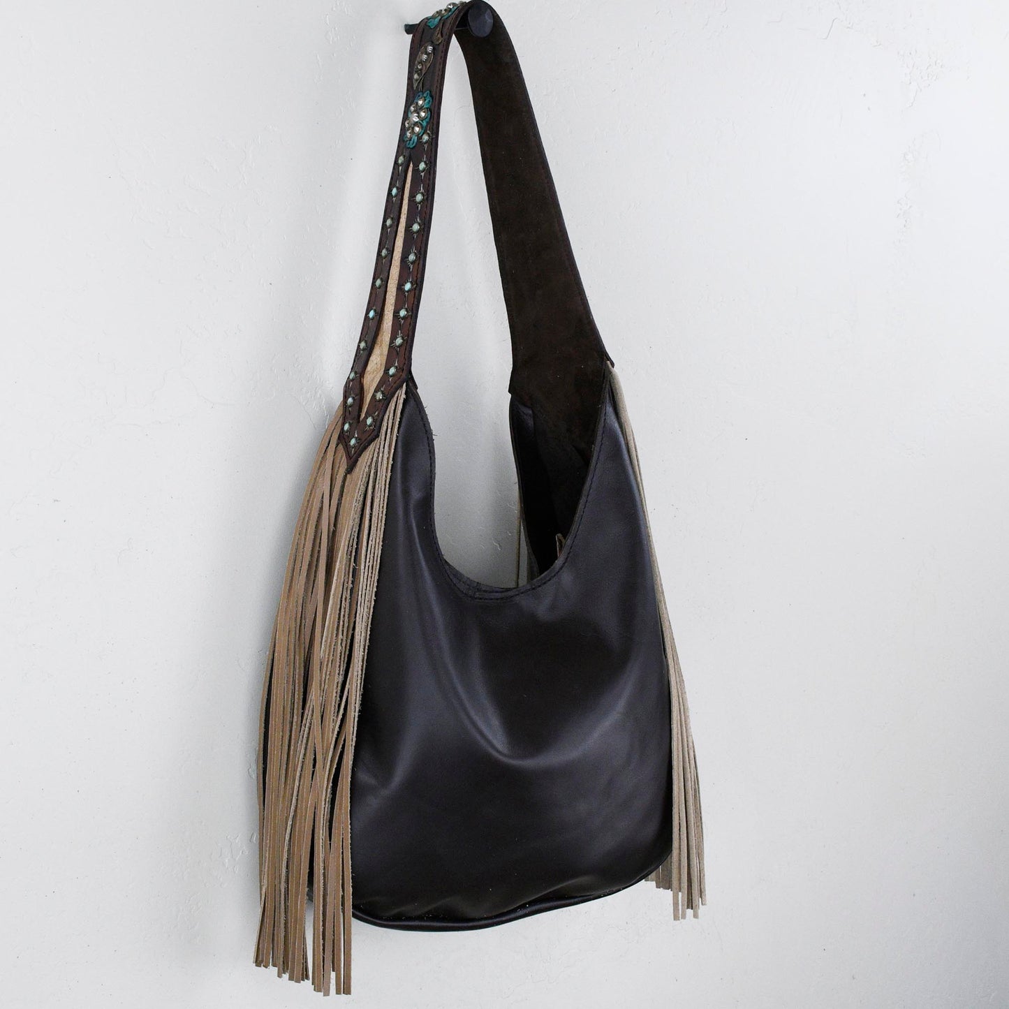 
                  
                    Marilyn bag #1248 by Heritage Brand with fringe details hanging on a white wall.
                  
                