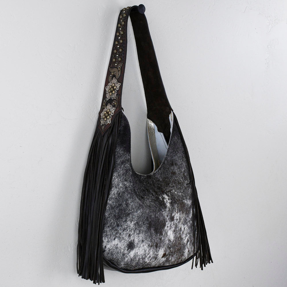 A Heritage Brand marilyn bag #1254 with tassels and a decorative strap hanging on a white wall.