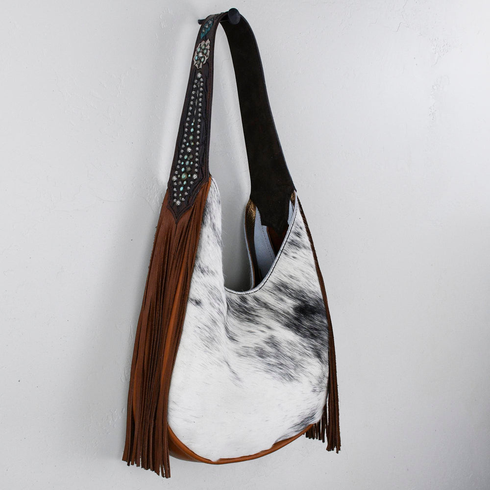 A Heritage Brand marilyn bag #1253 with fringe details hanging against a white wall.