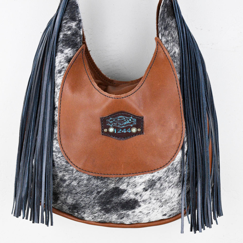 
                  
                    Heritage Brand's Marilyn Bag #1244, a Western style leather and cowhide shoulder bag with fringe detail and a decorative metallic plate.
                  
                