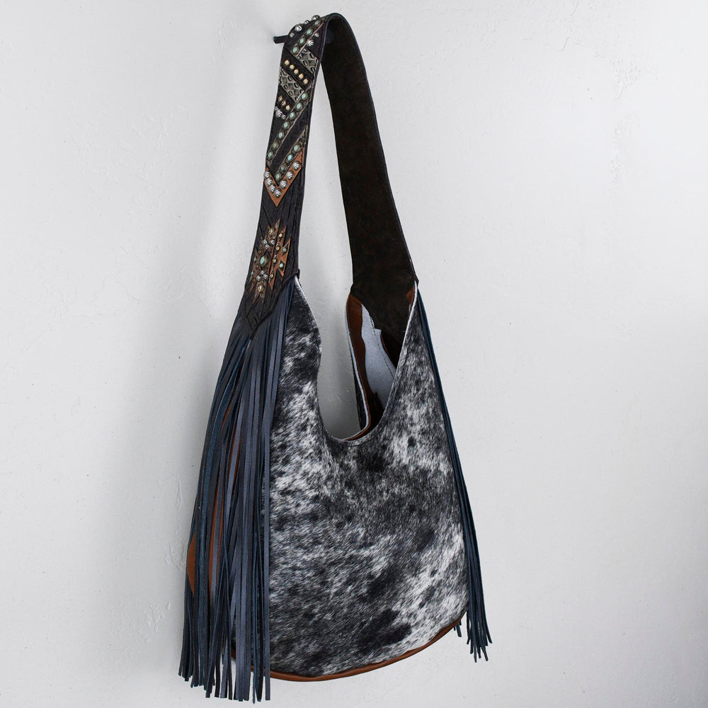 A Heritage Brand marilyn bag #1244 with fringe detailing hanging against a white wall.