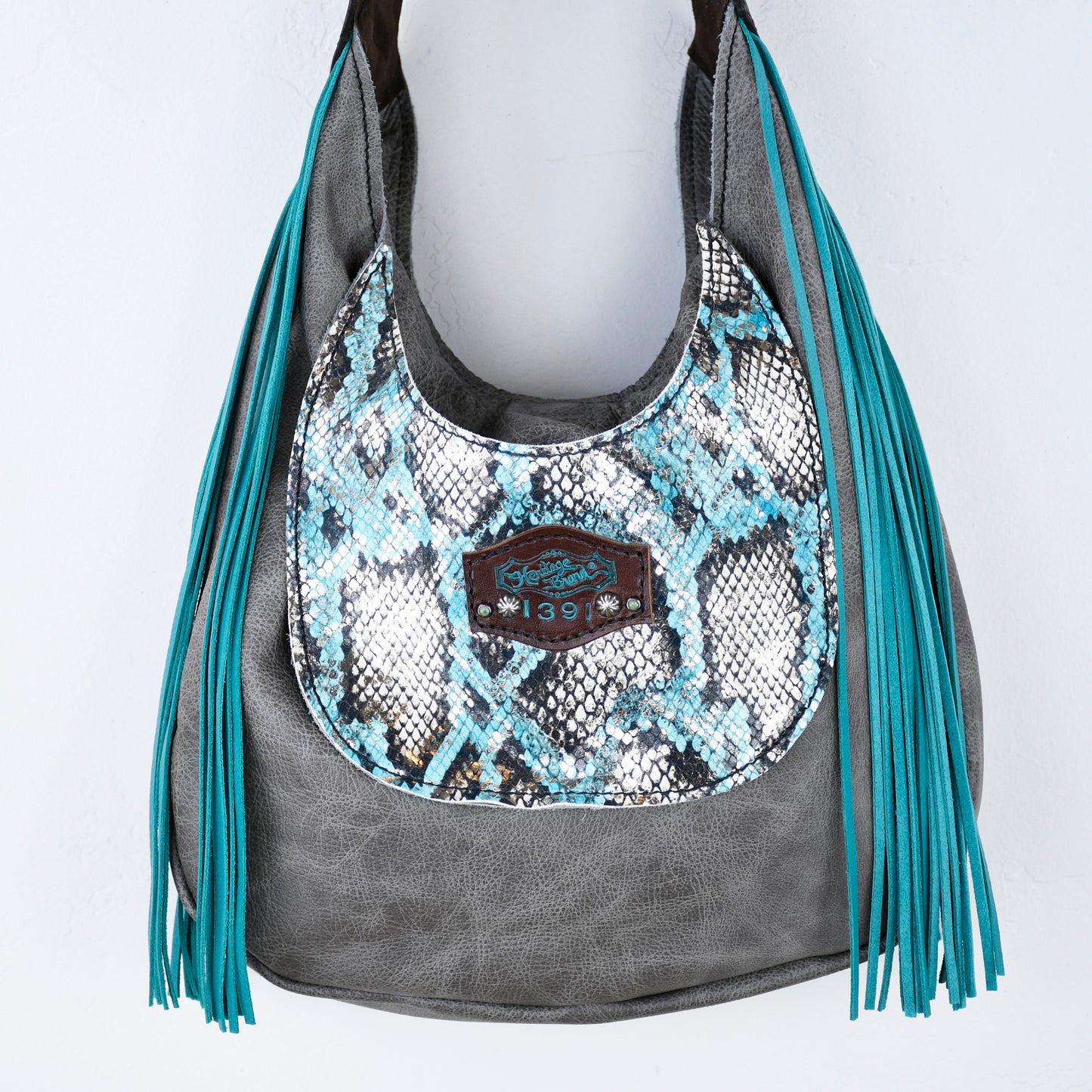 
                  
                    A turquoise and gray marilyn bag #643 with a snakeskin pattern and fringe detail by Heritage Brand.
                  
                