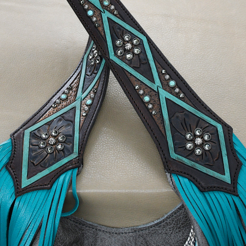 
                  
                    Close-up of a Heritage Brand marilyn bag #643 in turquoise and brown leather with decorative stitching and metal embellishments.
                  
                