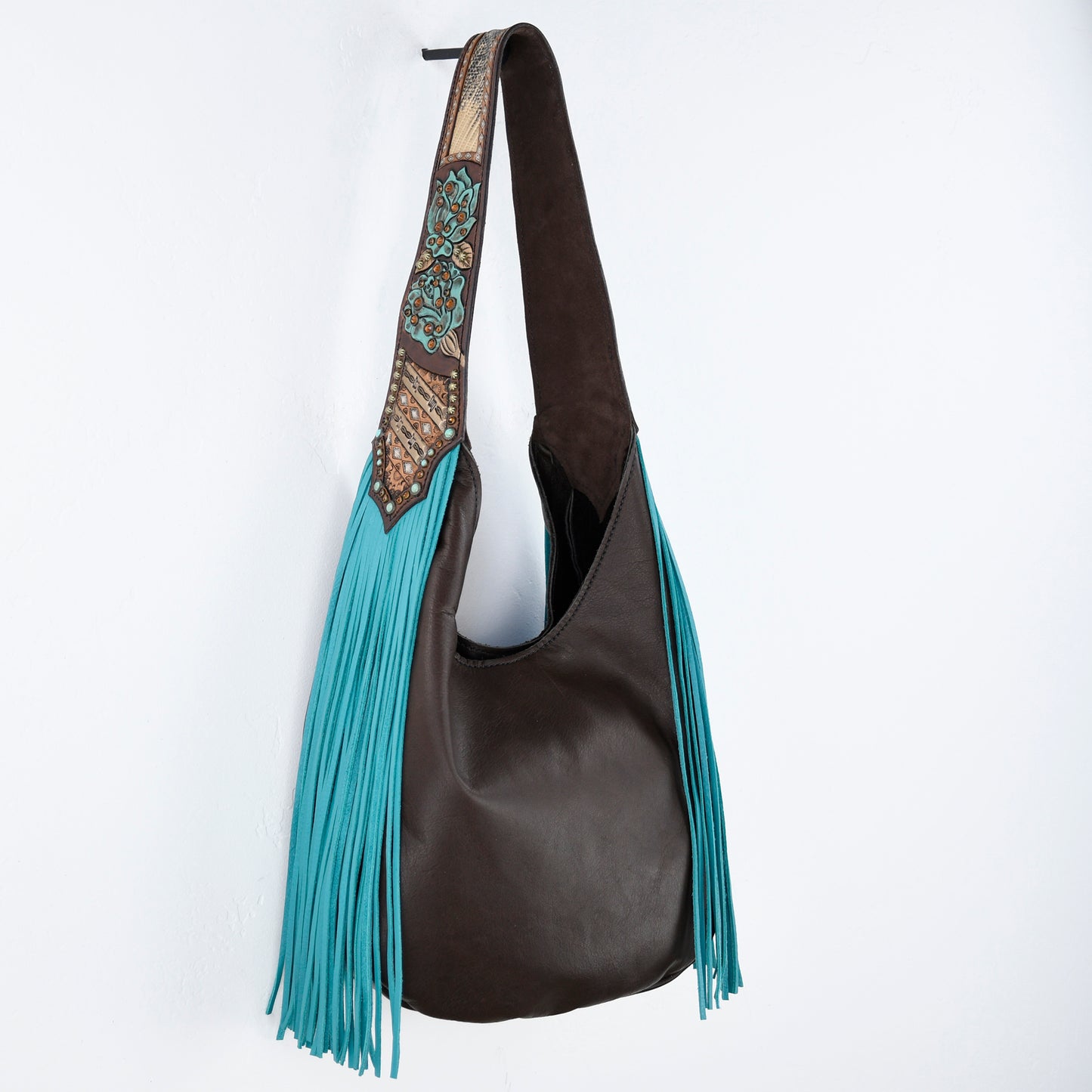 
                  
                    A brown leather Marilyn bag #658 with a decorative strap and blue fringe hanging against a white background from Heritage Brand.
                  
                