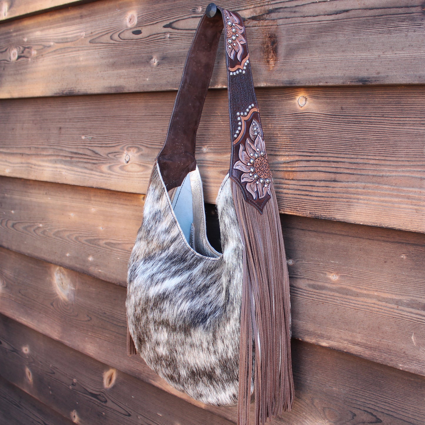 
                  
                    A Marilyn Bag #988 by Heritage Brand with leather fringe and embossed details hanging on a wooden wall.
                  
                