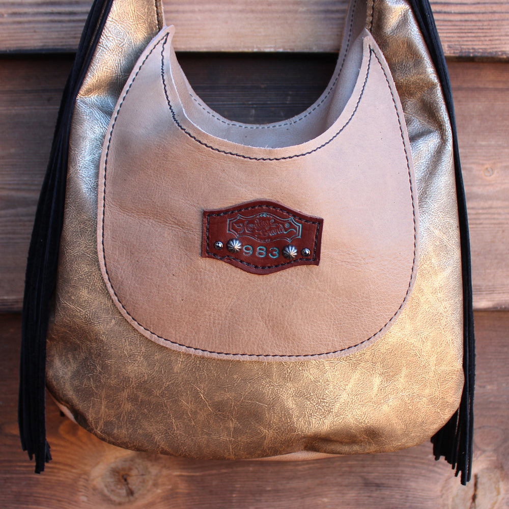 
                  
                    A bronze-colored leather Marilyn bag #983 with fringe details and a decorative metal emblem from Heritage Brand.
                  
                