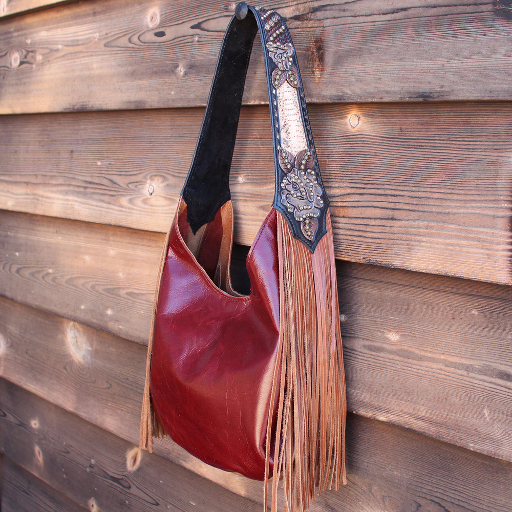 A Heritage Brand marilyn bag #975 with fringe and an ornately decorated strap hanging on a wooden wall.