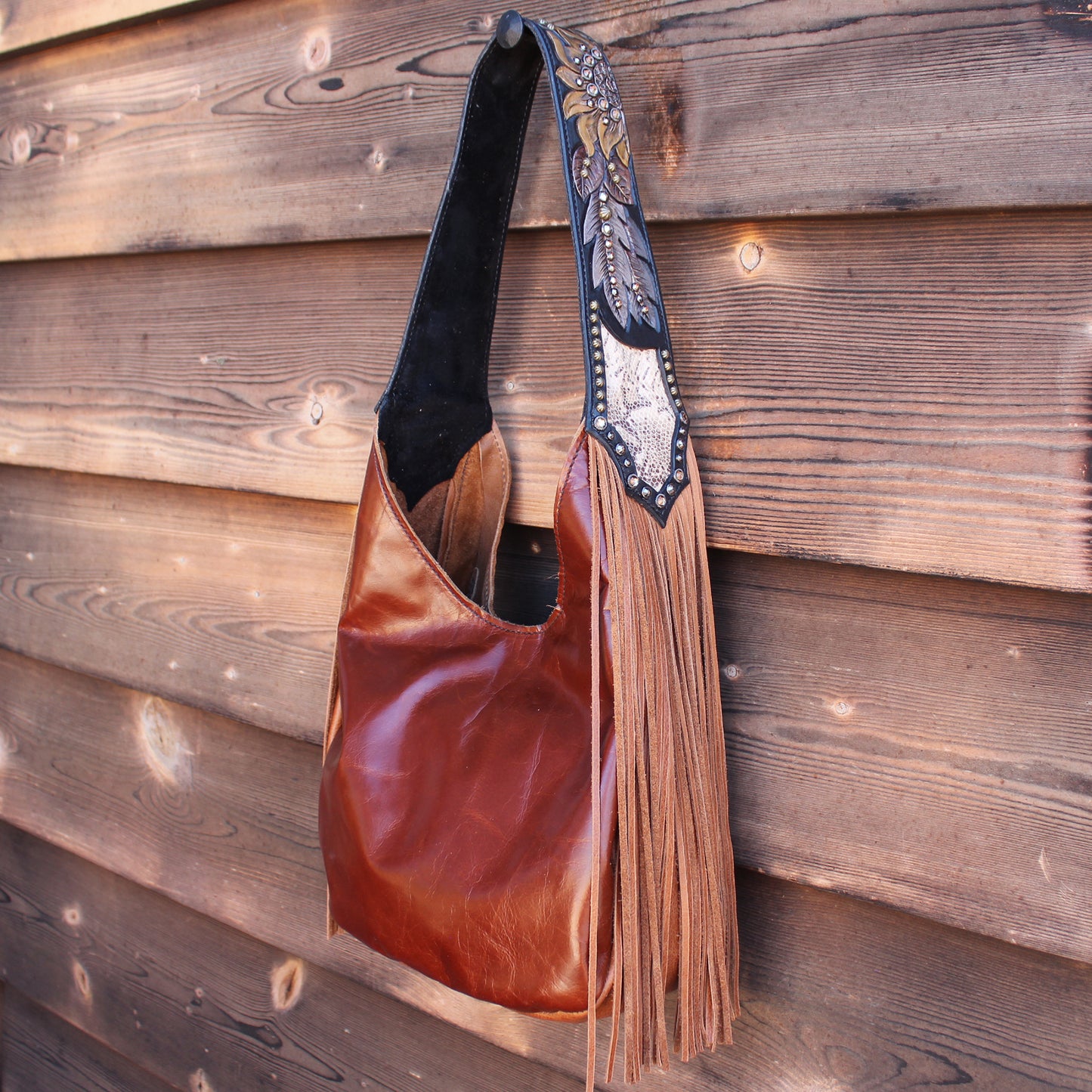 
                  
                    A Marilyn bag #974 by Heritage Brand, made of brown leather with a black strap and decorative fringe against a wooden background.
                  
                