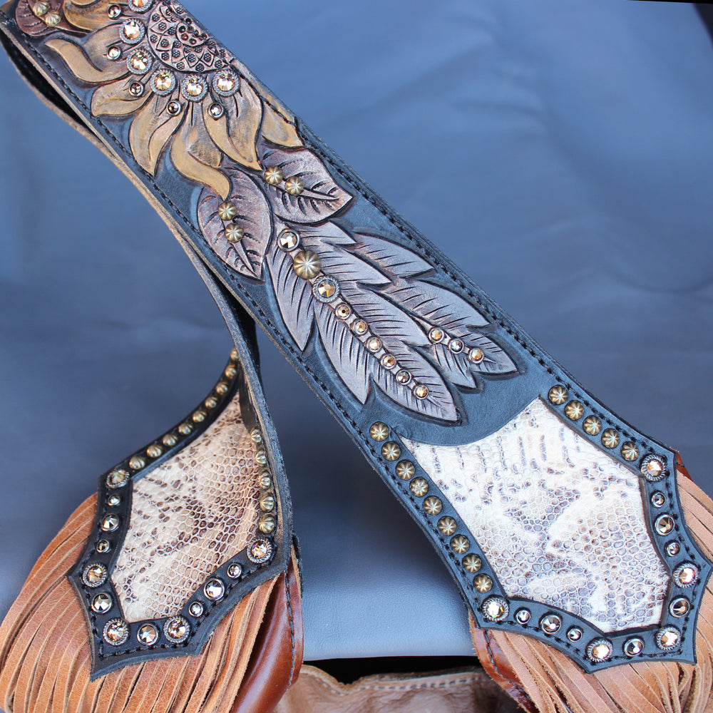 
                  
                    Ornate western-style Heritage Brand leather strap with embossed and studded detailing on a dark fabric background.
                  
                