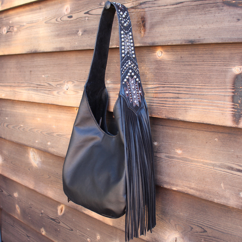 Marilyn bag #982 by Heritage Brand, a black leather shoulder bag with fringe and stud detailing, hanging on a wooden wall.