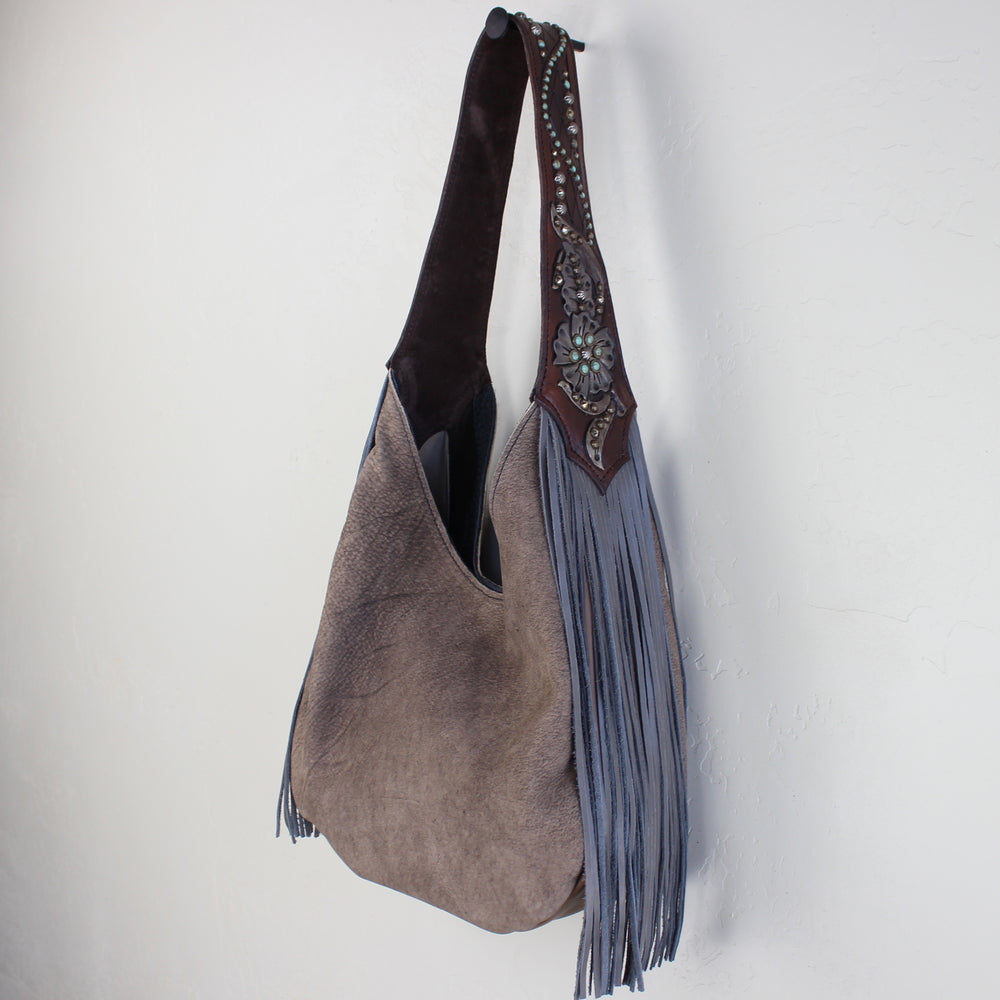 
                  
                    A Heritage Brand marilyn bag #1114 with fringe detailing hanging against a white wall.
                  
                
