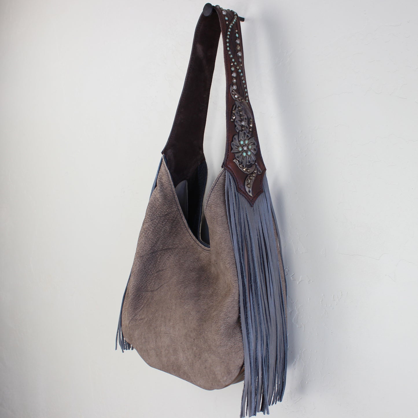 
                  
                    A Heritage Brand marilyn bag #1114 with fringe detailing hanging against a white wall.
                  
                