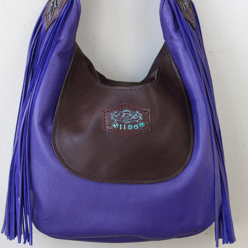 
                  
                    A purple leather marilyn bag #1186 with fringe details and center label on a white background by Heritage Brand.
                  
                