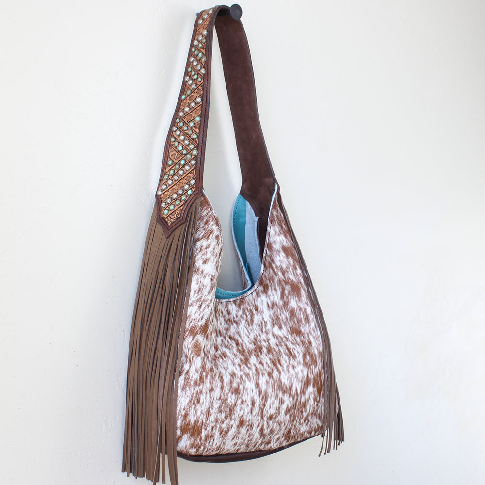 
                  
                    Brown and white cowhide Marilyn bag #1197 with fringe details and an embellished strap against a white background by Heritage Brand.
                  
                