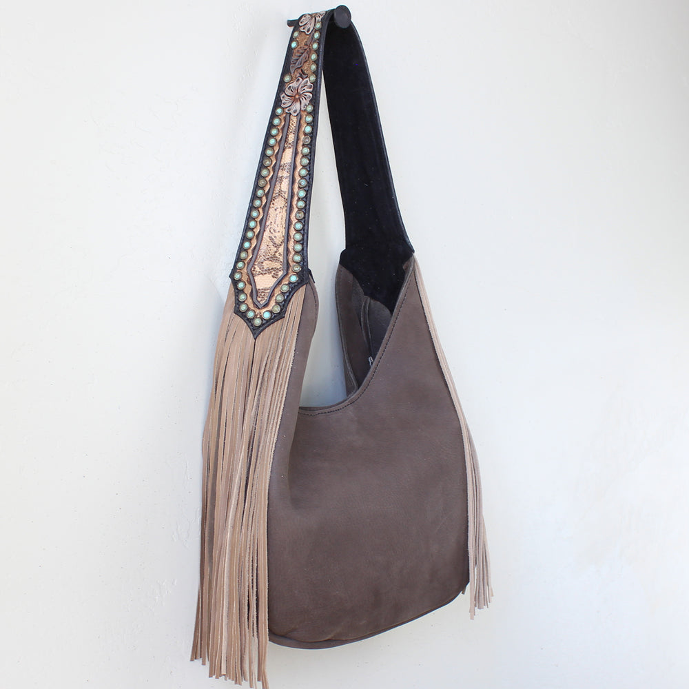 
                  
                    Heritage Brand brown suede Marilyn bag #1200 with decorative strap and fringe details hanging on a white wall.
                  
                
