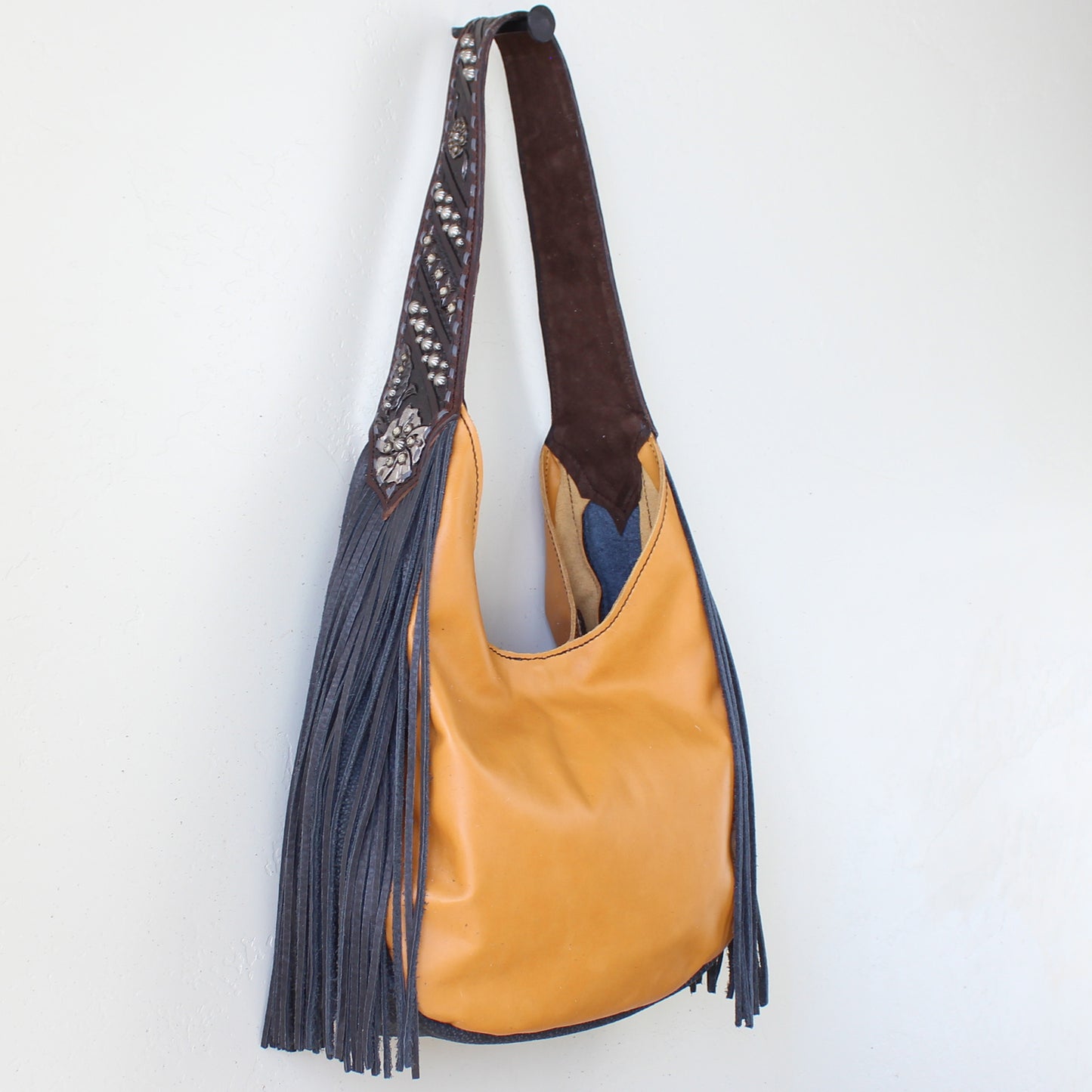 
                  
                    Brown and tan leather Marilyn Bag #1188 shoulder bag with fringes hanging on a white wall by Heritage Brand.
                  
                